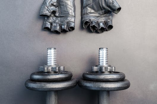 Black dumbbells and leather gloves on a workout mat ready for fitness training.