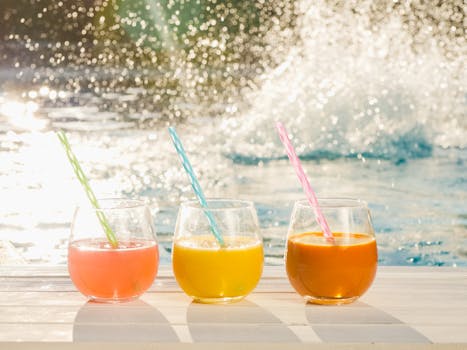 Colorful tropical fruit juices with straws beside a sunlit pool. Perfect summer refreshment.