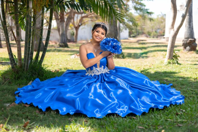 Beautiful young woman in a blue quinceañera gown sitting outdoors, embracing tradition and elegance.