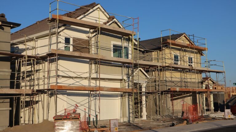 Scaffolded suburban homes under construction in Elk Grove, California during a sunny day.