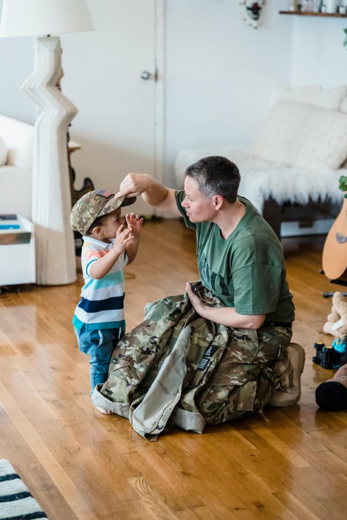 A father in military attire shares a tender moment with his child indoors.
